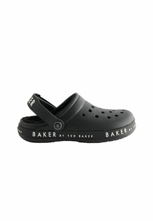 Černé boty ve stylu crocs vyrobené z hladké gumy s ventilačními otvory, nastavitelným zadním popruhem a bílým textovým logem podél podrážky.
