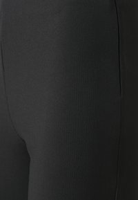 Leggings noirs côtelés à coupe près du corps, offrant une texture lisse et en matériau élastique qui procure de l'élasticité et du confort.