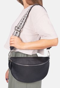 Schwarze Lederhandtasche in strukturierter, halbmöndiger Form. Verfügt über einen gemusterten, verstellbaren Trageriemen und einen silbernen Reißverschluss zum Verschließen.