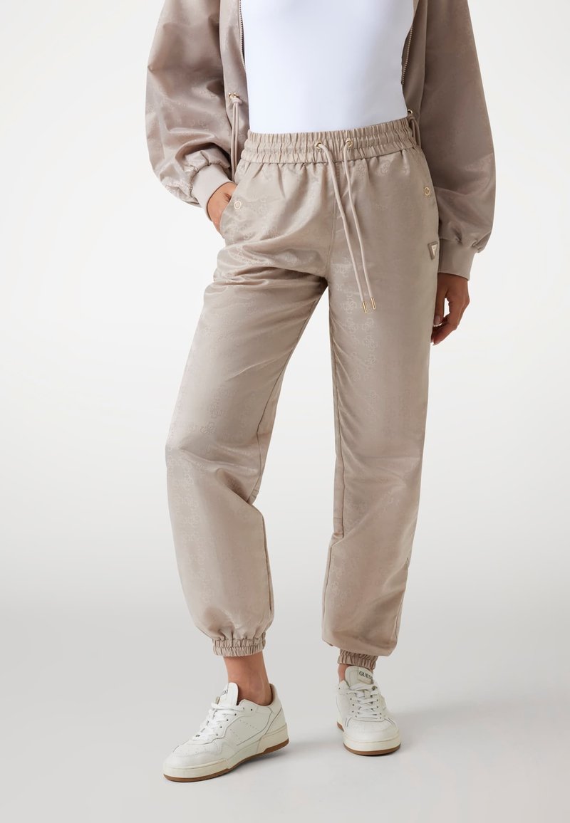 Beige jogger broeken van glanzende stof, met een elastische tailleband met trekkoord, geribbelde boorden en subtiele patroon details.