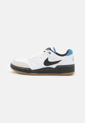 Zapatilla blanca con acentos negros, puntera gris, lengüeta azul en el talón y suela de goma. Presenta cuero texturizado y detalles cosidos.