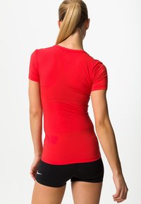 Punainen lyhythihainen urheilupaita, jossa on vartalonmyötäinen malli ja joustava kangas. Varustettu pyöreällä kaula-aukolla ja sileällä pinnalla.