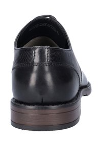 Zwarte leren dress-shoe met een gladde afwerking, textuuraccent, ronde neus en een bruine gestapelde hak. Achteraanzicht toont naaddetails.
