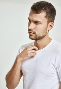 Tricou alb cu guler rotund, realizat dintr-un material neted, design ajustat, stil minimalist, purtat de un bărbat cu păr scurt, pe un fundal deschis.