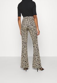 Pantaloni a zampa d'elefante con stampa leopardata in beige con macchie nere. Il tessuto appare liscio, la progettazione è a vita alta, completata da sandali neri con tacco.