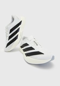 Paire de chaussures de running blanches Adidas avec des bandes noires, des lacets et des semelles épaisses et rembourrées sur un fond clair uni.