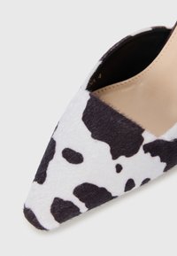 Chaussure à talon aiguille en tissu imprimé noir et blanc de vache, avec une surface texturée et un design élégant.