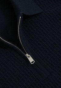 Tmavomodrý textúrovaný pulóver s polovičným zipsom. Obsahuje strieborný zips a štruktúrovaný golier. Mäkka, pletená látka.
