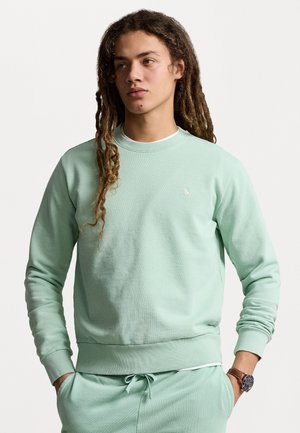 Sweatshirt vert menthe en tissu doux avec des poignets et un ourlet côtelés, arborant un petit logo brodé sur la poitrine. Assorti à un pantalon de jogging.