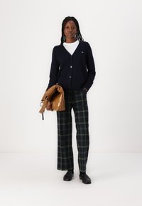 Navy cardigan with buttons, white t-shirt underneath, green and black plaid wide-leg pants, and a shiny brown bag. Black shoes.