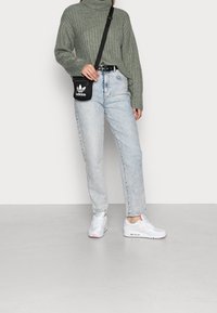 Grön ribbad polotröja, ljus tvätt högmidjade jeans, svart axelremsväska med Adidas-logotyp, och vita sneakers med rosa detaljer.