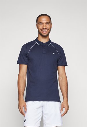 Marine blauwe polo met een knoopsluiting met twee knopen, witte piping langs de kraag en mouwen, en een klein logo op de borst. Draagt samen met witte shorts.