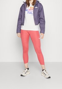 Chaqueta impermeable morada, camisa blanca con logo colorido, mallas rosas y zapatillas beige. Textura suave, diseño ajustado, con cremalleras en las mallas.