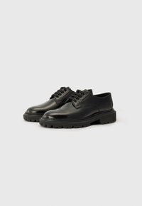 Chaussures en cuir noir avec une finition lisse, bout arrondi, design à lacets et semelle en caoutchouc épaisse présentant un motif de traction.