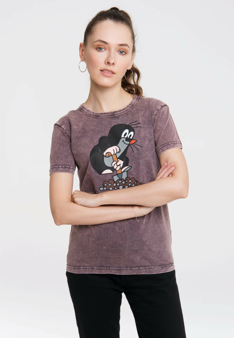 Grafisches T-Shirt aus verblasstem lila Stoff mit einem Cartoon-Design von einem Maulwurf. Kurze Ärmel, Rundhals-Ausschnitt und lockere Passform. Sichtbare schwarze Hose.