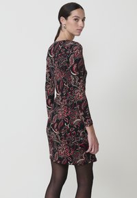 Vestido negro de manga larga con un estampado floral en rojo y dorado. El diseño ajustado presenta un escote redondo y un dobladillo a la altura de la rodilla.