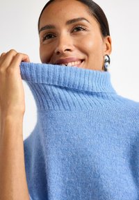 Maglione dolcevita azzurro chiaro in tessuto morbido e lavorato a maglia con colletto a costine. Texture visibile, vestibilità comoda e aspetto caldo.