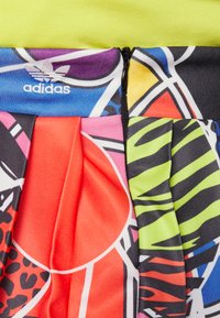 Kolorowa, plisowana tkanina z czerwonymi, różowymi i zielonymi wzorami oraz czarnymi akcentami; zamek błyskawiczny na górze; widoczne logo Adidas.