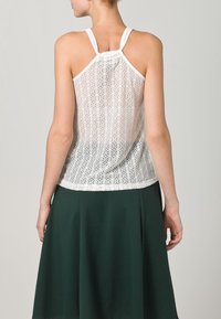 Top in pizzo bianco con texture a motivo e spalline regolabili, abbinato a una gonna svasata verde scuro. Vista posteriore mostrata.