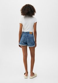 Shorts de mezclilla, de color azul claro, de cintura alta con dobladillos enrollados, que cuentan con dos bolsillos traseros y una patch de cuero marrón en la cinturilla.