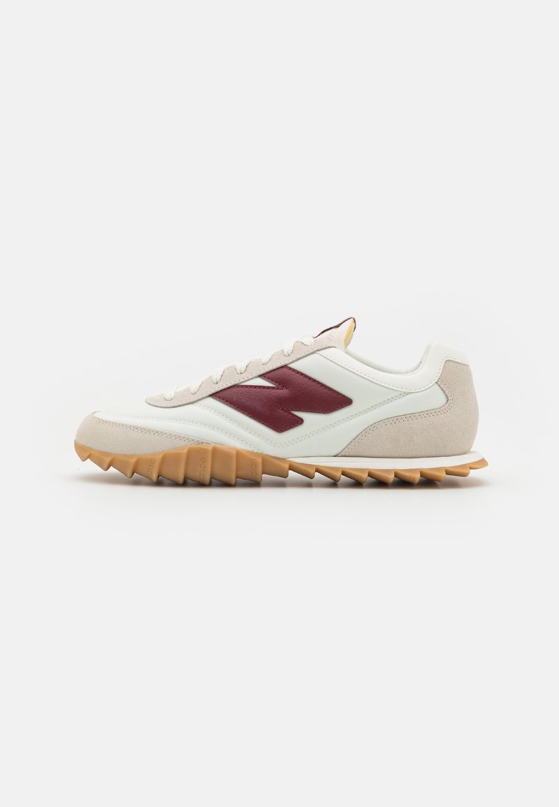White leather sneaker with a maroon logo, grey suede accents, and a textured gum rubber sole with pronounced lugs for traction.