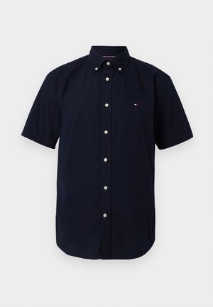 Marineblå kortermet skjorte med knapper laget av bomull. Har en klassisk krage med hvite knapper og en liten logo på brystet.