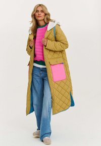 Khaki prešívaný dlhý kabát s ružovou kapsou, sivou kapucňou a modrou podšívkou. Spárované s prúžkovaným ružovým sveterom, modrými džínsami a sivými topánkami.