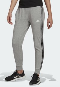 Grå träningbyxor i en bomullsblandning, med tapered passform, svarta sidostreck och elastiska muddarna. Adidas-logotyp på vänster höft.