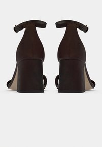 Καφέ καστόρινες γόβες με ψηλό τακούνι που διαθέτουν κλειστή φτέρνα, λουράκι στον αστράγαλο και στρογγυλή μύτη με φαρδύ τακούνι μπλοκ.