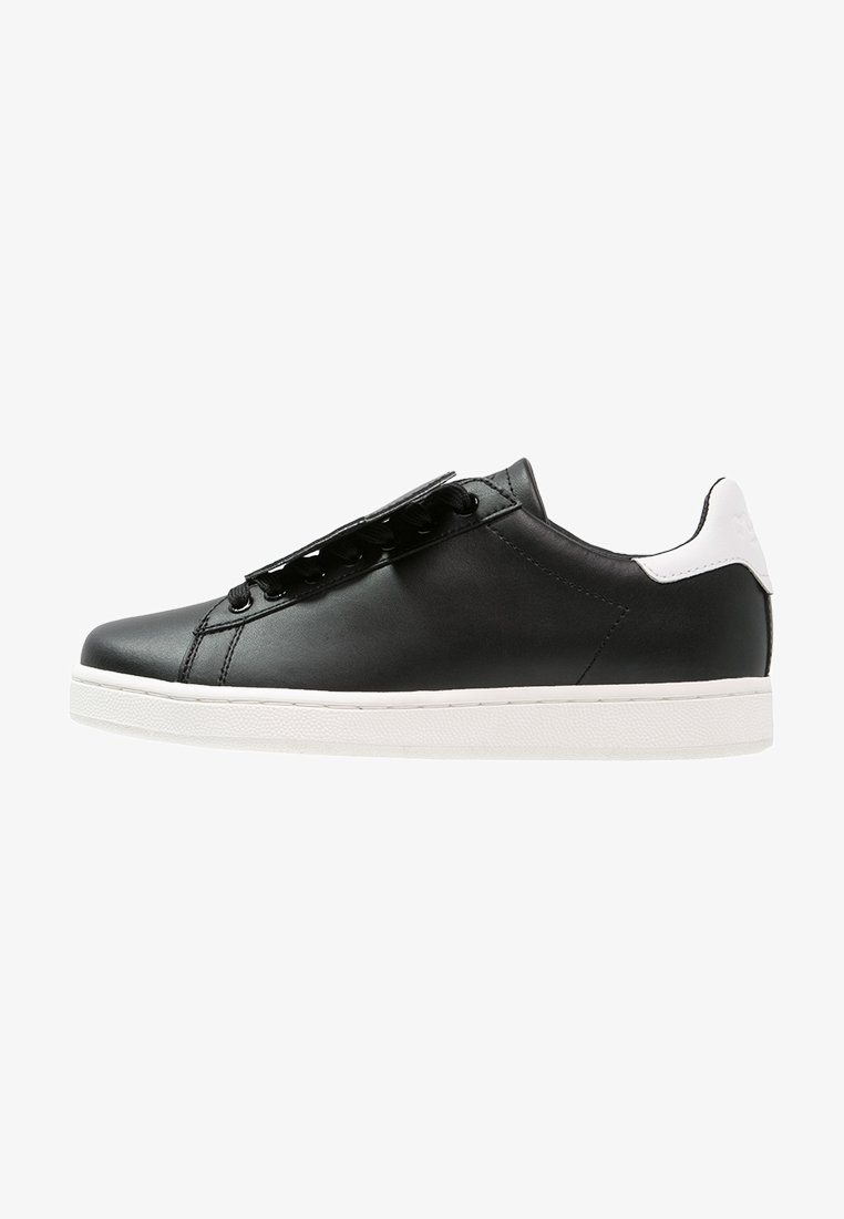 Black leather sneaker with a smooth finish, featuring a white heel accent and black laces. The sole is white and textured for grip.