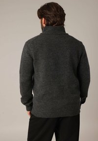 Pull en tricot gris foncé avec un col montant, des poignets et un ourlet côtelés. Texture douce, design ajusté avec un corps légèrement ample.