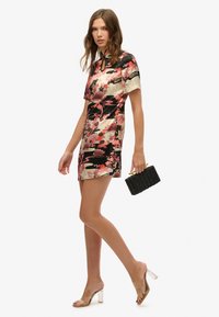 Vestido mini floral con patrones en negro y rosa, mangas cortas y escote en forma de ojo de cerradura. Combinado con tacones transparentes y un bolso de mano negro tejido.