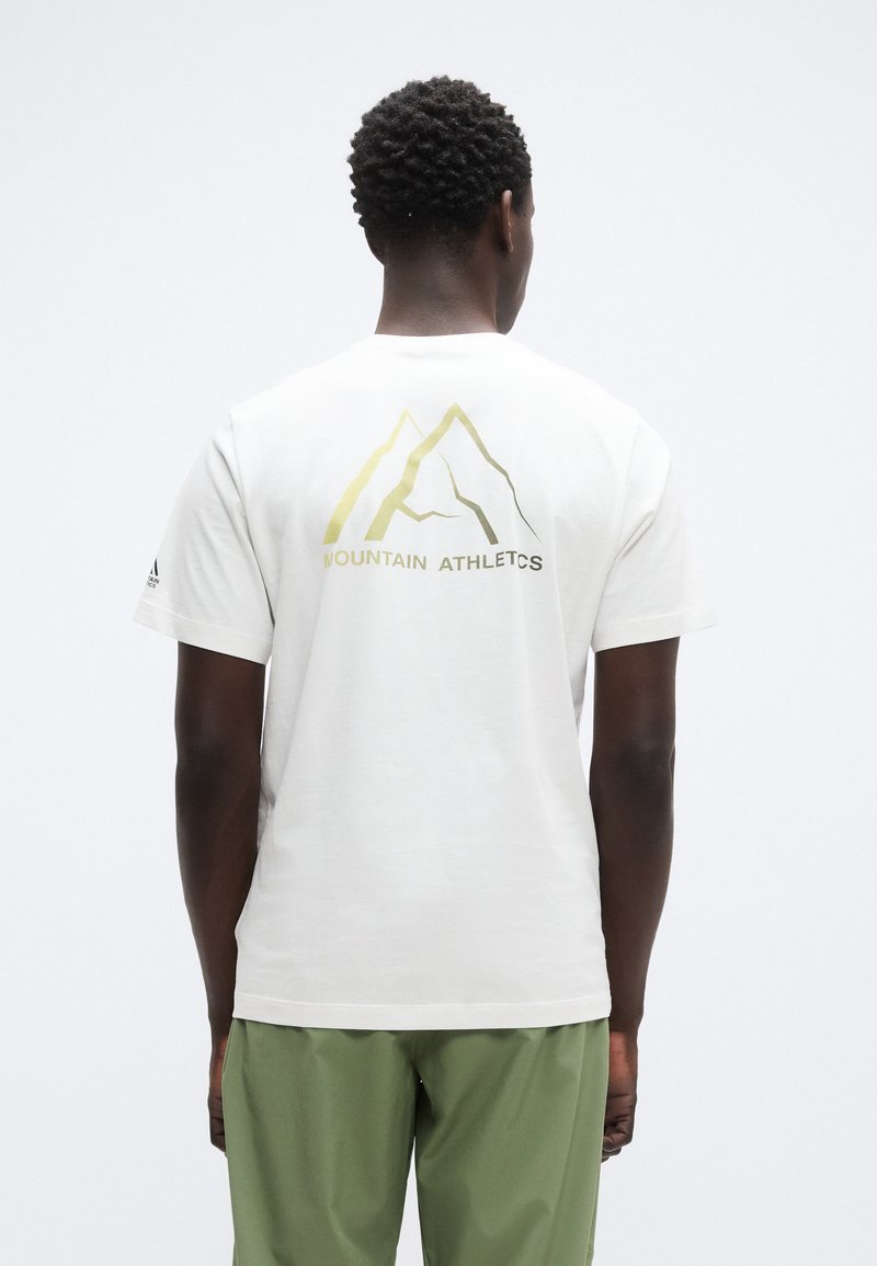 Λευκό βαμβακερό μπλουζάκι με χρυστό γραφικό βουνό και κείμενο "MOUNTAIN ATHLETICS" στην πλάτη. Κοντά μανίκια, άνετη γραμμή.