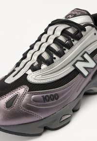 Sneaker sportivo nero e argento con accenti viola. Presenta materiali in rete e sintetici, design con lacci e un notevole marchio "1000" sul lato.