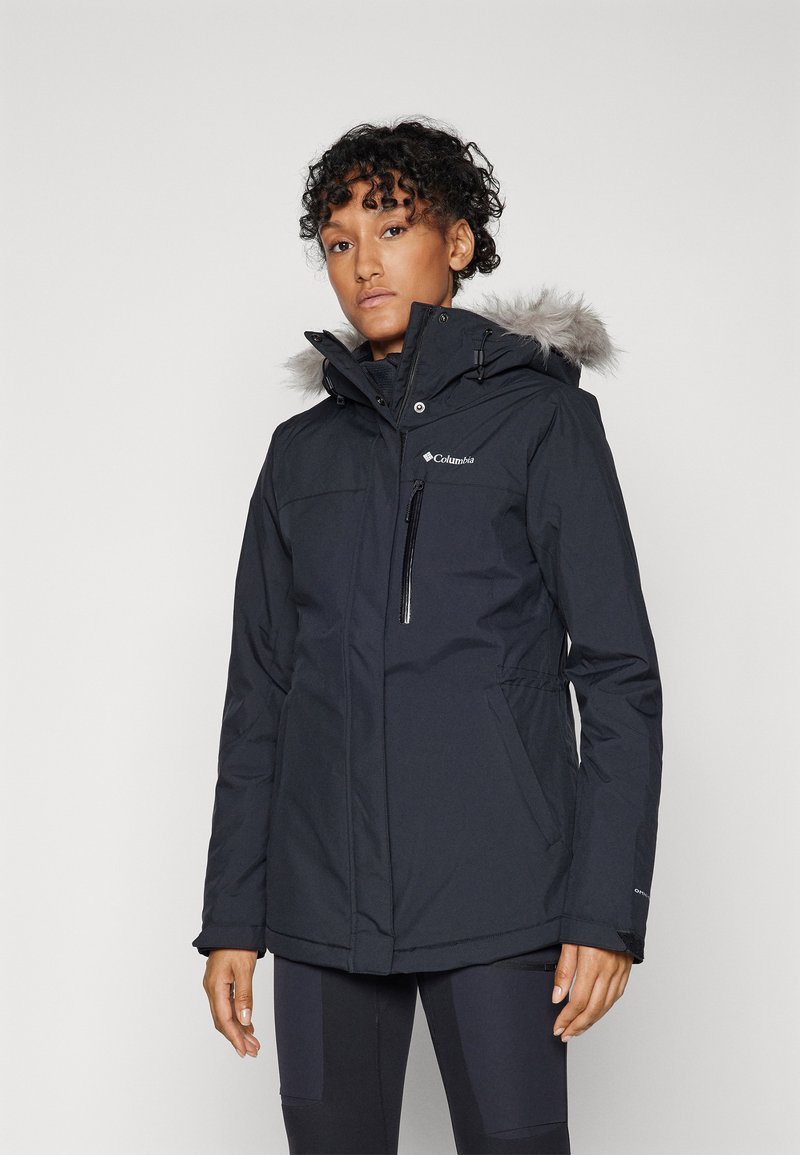 Chaqueta negra con capucha, hecha de material impermeable, con un borde de pelo, bolsillos con cremallera, puños elásticos y una cintura ajustada para mantener el calor.