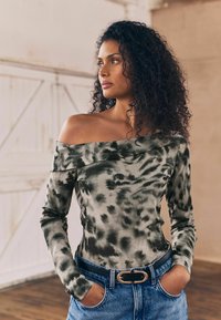 Langærmet off-shoulder top i et grå og sort tie-dye mønster, lavet af blødt stof. Sammen med højtaljede blå jeans og et sort bælte.