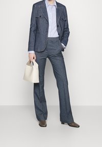 Džínový oblek s modro-bílou pruhovanou košilí, širokými kalhotami a béžovou kabelkou. Obsahuje kontrastní švy a přiléhavý střih.