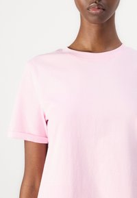 Lys rosa bomulls t-skjorte med rund hals, korte ermer og en glatt tekstur. Ingen synlige mønstre eller logoer.