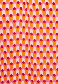 Toisto kuvio oransseista ja valkoisista päällekäisistä soikista, joissa on pieniä punaisia puoliympyröitä vaaleanpunaisella taustalla, kangas hieman taittunut keskeltä.