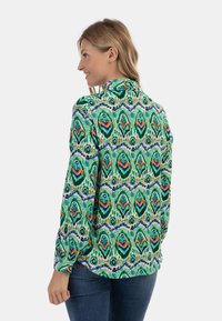 Camicia verde a motivi con design floreale in tonalità blu, arancio e bianco; maniche lunghe; e colletto con bottoni.