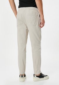 Pantalones cargo beige claro con cintura elástica, bolsillos laterales y traseros, piernas ajustadas y una textura de algodón suave, combinados con zapatillas negras.