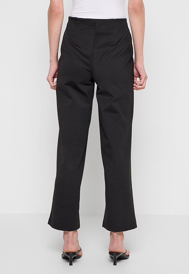 Czarne, wysokie spodnie o szerokich nogawkach, z gładką fakturą i minimalnymi detalami przeszycia na końcu nogawek.