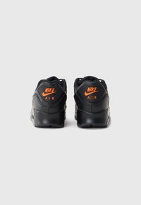 Adidașii negri Nike Air au un superior din piele netedă, un logo portocaliu proeminent pe călcâi, o talpă texturată și glezne căptușite pentru confort.