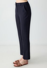 Marineblauwe broek met een rechte pasvorm, zijzakken, voorkruiken en een zachte textuur, gecombineerd met bruine sandalen met een geweven ontwerp.