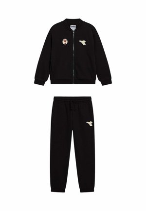 Giacca nera con zip e pantaloni con vita elastica con loghi beige sul petto e sulla coscia, esposti su sfondo bianco.