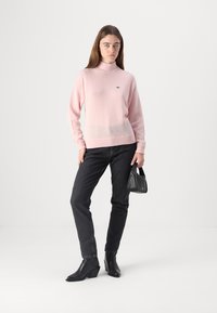 Ljusrosa polotröja med en mjuk textur, bärs tillsammans med mörka jeans och svarta klackboots, håller en liten svart handväska.