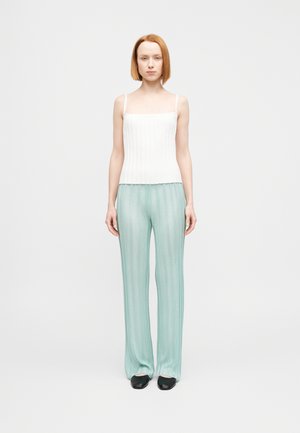 Canotta bianca a coste abbinata a pantaloni plissettati color menta, leggeri e fluidi. La modella indossa scarpe nere; il tessuto ha una consistenza liscia e morbida.