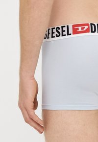 Gaiši zili bokserbiksītes no mīksta auduma, ar melnu un baltu elastīgu jostu ar logotipu. Vienkāršs dizains bez rakstiem.