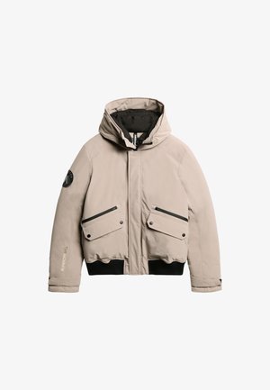 Chaleco acolchado beige con capucha, forro negro, dos bolsillos frontales con solapa y dobladillo acanalado. Presenta un parche de logo y bolsillos con cremallera.