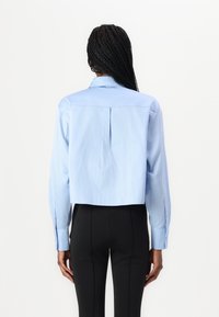 Camicia button-up azzurro chiaro a maniche lunghe, con dettaglio di piega sul retro e pantaloni neri aderenti. Tessuto morbido, design classico del colletto.